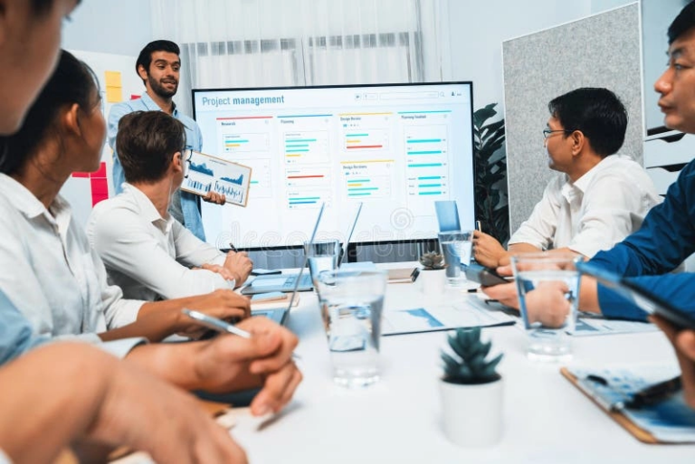 Business team collaborating in a project management meeting with visual progress tracking on a large screen.