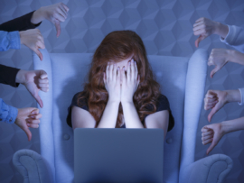 Girl with laptop covering face, around hands holding thumbs down.