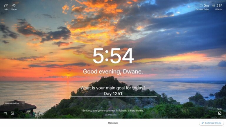 A stunning panoramic view of a tropical bay at sunset, seen from a high vantage point on a lush, green hill. The sky is filled with dramatic clouds, brilliantly lit with hues of orange, yellow, and pink by the setting sun on the horizon. The calm ocean below is dotted with numerous small boats, creating a serene and picturesque scene. The location is Quepos, Costa Rica.